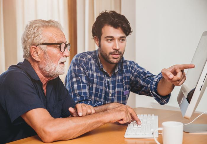 Young man helping older man on desktop computer