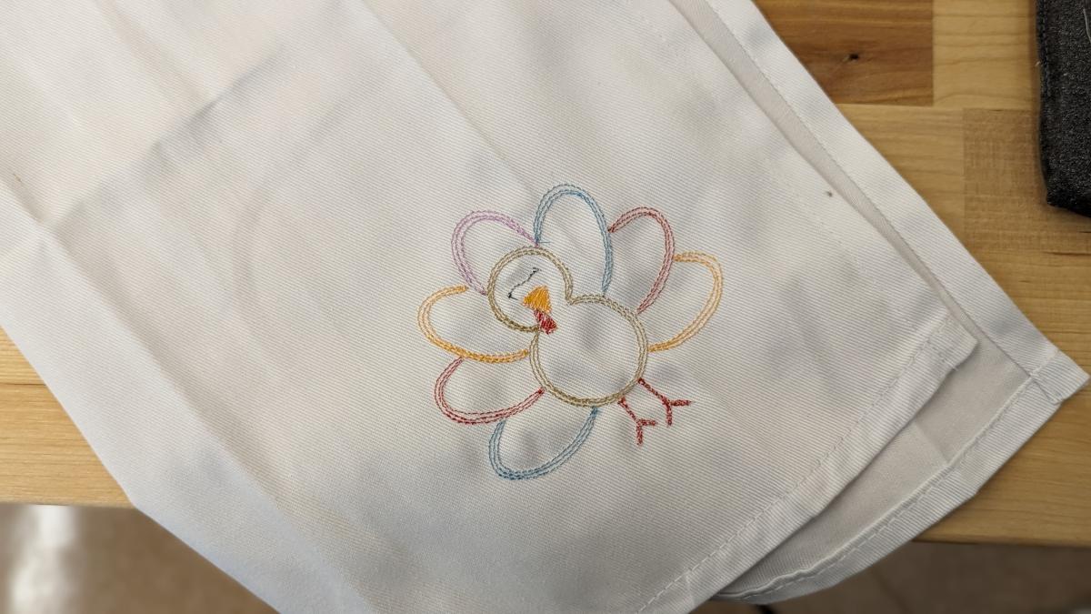 Photo of a white napkin with a multi-colored turkey embroidered on the front